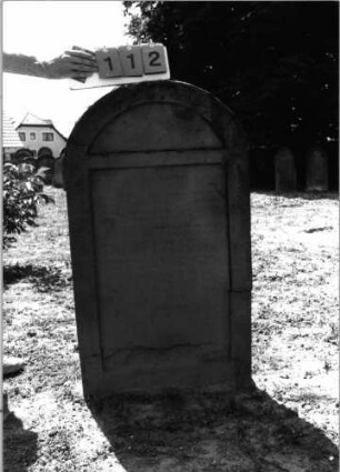 Grabstein 112 (Index: 99798107) Material: Sandstein, rot Zustand: leicht verwittert Maße HxBxT: 117x61x14 cm Beschreibung: Stele, Segmentbogenabschluß: Grabstein 112