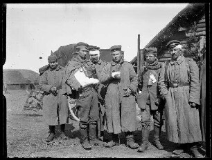 Unbekannte Ortschaft [Litauen/Weißrussland/Ukraine?]: verletzte Soldaten mit Pickelhaube, Schirmmütze und Tellermütze und Kopf, Arm- und Handverbänden im Freien vor Holzhäusern