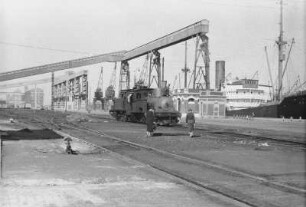 Hafen : Bahnschienen und Lokomotive in einem Hafen; davor zwei Frauen