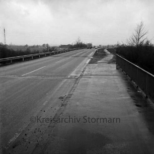 Ostring: rechts Geländer von Straßenüberführung: an rechter Straßenseite Fahrradweg, an linker Straßenseite Leitplanke: hinten Straßenkurve, Lkw, Autos: im Hintergrund Felder, Strommasten