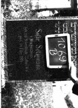 Grabstein 1069 (Index: 100104105) Material: Granit Zustand: gut erhalten Maße HxBxT: 172x48x17 cm Beschreibung: aufgesockelte Stele, Schulterbogenabschluss, eingeritzte Voluten, Akanthusblätter und Mohnkapseln Symbolik: Akanthusblätter, Mohnkapseln: Grabstein 1069B