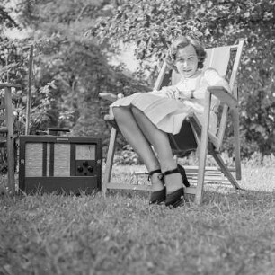 Elisabeth Gremmler sitzt in einem Klappstuhl im Garten, neben ihr steht ein Rundfunkempfänger