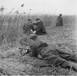 Deutsche Demokratische Republik. Grenze zwischen BRD und DDR. Offizier und Grenzpolizist bei einer Lagebesprechung mit Karte im Gelände, abseits zwei Grenzposten zur Sicherung des Abschnittes