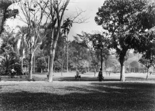 Parkanlage : Ein Park mit Grünflächen und Bäumen. In der Bildmitte drei Personen mit Gießkannen.