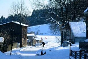 Holzscheune, Gärten und Häuser; rodelnde Kinder am Waldrand