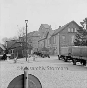 Klosterstraße, Kreuzung nach links Matthias-Claudius-Straße, nach hinten Ahrensböker Straße: Kopfsteinpflaster, Verkehrsinsel mit Straßenlaterne, Wegweiser nach Hamburg, Poller: drei Lastwagen mit Anhängern: Bildmitte hinten Claudius-Mühle, rechts Verwaltungsgebäude der Claudius-Mühle: links Kocksche Schmiede, Baum, Mann, Traktoranhänger: im Vordergrund Verkehrsschild