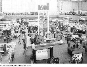 Raumaufnahme mit Werbeträger und Ausstellungskojen. Mitteltrakt der Ausstellungshalle mit Messebesuchern