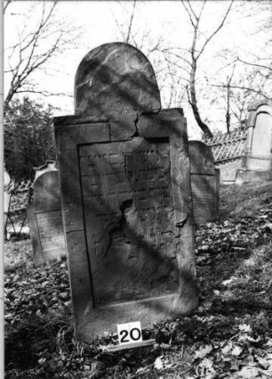 Grabstein 20 (Index: 100080848) Material: Sandstein Zustand: gebrochen, abgeblättert mit Textverlust Maße HxBxT: 139x60x10 cm Beschreibung: Stele, eingezogener hufeisenförmiger Abschluß, eingetieftes Schriftfeld rechteckig: Grabstein 20
