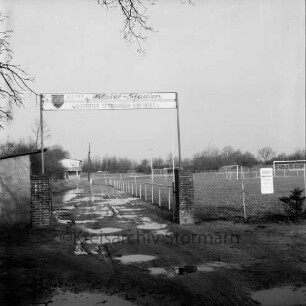 Sporteinrichtungen: Weg am Sportplatz: Sportplatz "Kleines Alster-Stadion" des Wilstedter Sportvereins von 1958 e. V.: vorn Eingangsbereich mit Wasserpfützen auf Weg: rechts Sportplätze: links Holzschuppen: dahinter Sportlerheim: hinten Bäume