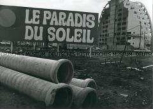 Im Vordergrund Röhren, dahinter ein Schild mit der Aufschrift "Le Paradies Du Soleil", dahinter eine halbkreisförmige Baukonstruktion (Altersgruppe 18-21)