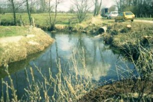 Burg Stegen: ehemaliger Standort (im Hintergrund rechts): vorne Alster, an Ufer Einlaufrohr: hinten rechts Wirtschaftsweg, parkende Autos, Lkw