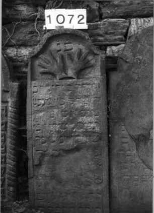 Grabstein 1072 (Index: 99630575) Material: Sandstein Zustand: stark abgeblättert, verwitt, Textverlust Maße HxBxT: 104x41x9 cm Beschreibung: Stele mit Konvexbogenabschluß Symbolik: segnende Hände: Grabstein 1072