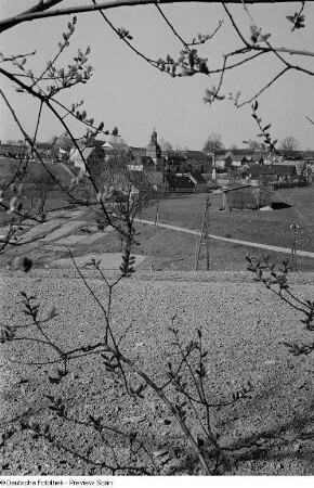 Blick durch Zweige auf ein Dorf mit Kirche (vermutlich in Thüringen)