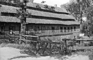 Drahtmühle: vorn Weg: dahinter Zaun und Bäume: rechts Warnschild an Mast