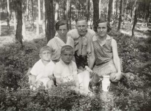 Drei Erwachsene und zwei Kinder im Wald sitzend