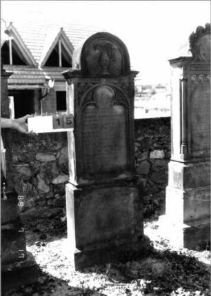 Grabstein 15 (Index: 99797968) Material: Sandstein, weiß Zustand: leicht verwittert Maße HxBxT: 178x60x21 cm Beschreibung: Stele, eingezogener Rundbogenabschluß, getreppter Sockel Symbolik: Levitenkanne, Ranken, Dreipaßbögen: Grabstein 15