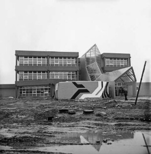Schulzentrum Reinbek: Mühlenredder: Hauptschule [später: Hertzig-Schule, dann zusammen mit Realschule Reinbek Gemeinschaftsschule Reinbek]: Neubau: Einweihung: Außenansicht mit Glaseingang und Pausenhalle sowie Kunst am Bau mit Pop-Art-Gemälde: hinten rechts im Eingang Personen: vorn Wasserpfützen in unbefestigtem Außengelände