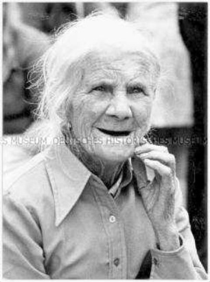 Gesicht, Schultern und Hand einer alten, lächelnden Frau mit weißen Haaren