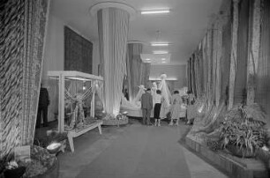 Besucher der Leipziger Herbstmesse 1955 betrachten drapierte Stoffbahnen