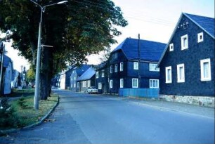 Straße mit Häuserzeile; in der Mitte Grünstreifen, dahinter parallele Straße und Häuserzeile