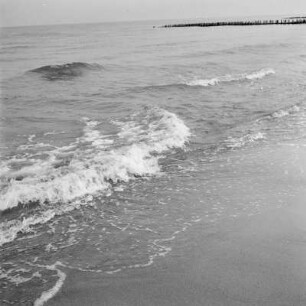 Wellen am Strand, im Hintergrund ein Wellenbrecher
