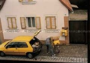 Postbote beim Beladen seines Fahrrades vor einem Haus (Altersgruppe 14-17)