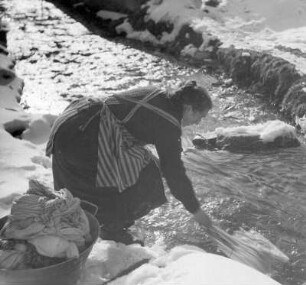 Winterbilder. Frau beim Wäschewaschen an einem Bach im Schnee
