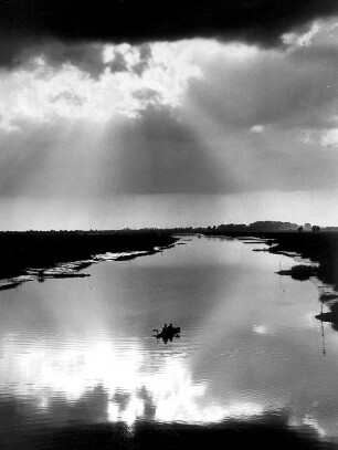 Impression. Die Sonne bricht durch die Wolken und spiegelt sich in der Süderelbe. Ein Ruderboot befindet sich auf dem Gewässer