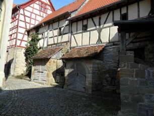 Kirchhof im Norden-mittig-mit Gaden (Kirchhofmauer mit Wehrgang als Außenmauer - Gaden mit Fachwerkobergeschoß sowie vorgebauten Kellereingängen)