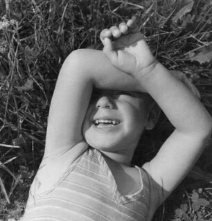 Kinderbilder. Kleinkind, auf einer Wiese liegend, die Arme vor dem Gesicht