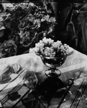 Stilleben. Glasschale mit Weintrauben, gespiegelte Rosen im Hintergrund