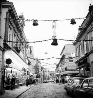 Mühlenstraße mit Adventsbeleuchtung: Passanten und parkende Pkw, links das Kaufhaus Nickel, rechts Einmündung der Hindenburgstraße, Blick Richtung Süden