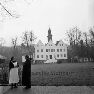 Kloster Nütschau: Herrenhaus: Nordfront mit Außentreppe: davor Rasenfläche: rechts und links Bäume: vorn links Pater Subprior Matthäus Buß und Clemens-Schwester im Gespräch