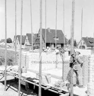 Wohnungsbau: Claudiusweg: Wohngebiet Kellerberg-Süd: Bau von Wohnhäusern: Arbeiter beim Hochziehen der Grundmauern: dahinter fertiggestellte oder sich im Rohbau befindende Einfamilienhäuser