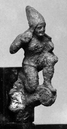 Applik eines etruskischen Helms: Kleines Figurchen eines unbärtigen, knienden Bogenschützen mit hohem, spitzen Helm; auf einer Volute