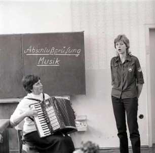 Musikprüfung : Großbardau. EOS Schülerin mit FDJ Hemd bei der Musik Abschlussprüfung. Sie singt während sie von der Lehrerin auf dem Akkordeon begleitet wird