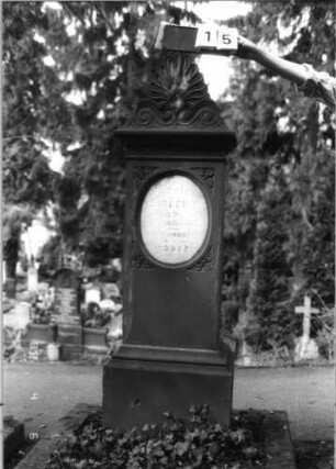 Grabstein 15 (Index: 99792901) Material: Sandstein und Marmor Zustand: Sprünge, leicht verwittert Maße HxBxT: 175x50x34 cm Beschreibung: Stele, Sockel profiliert, Giebel mit Akroter, Schriftfeld eingetieft, stehendes Oval, Textplatte eingesetzt Symbolik: Efeublätter Besonderheit: Schrift vergoldet: Grabstein 15
