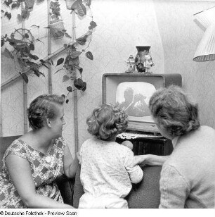 Zwei Frauen mit Kind vor laufendem Fernsehgerät sitzend