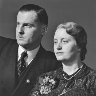 Portrait eines älteren Paares, der Mann trägt einen Zweifinger- oder Hitlerbart und eine Anstecknadel mit Hakenkreuz am Revers