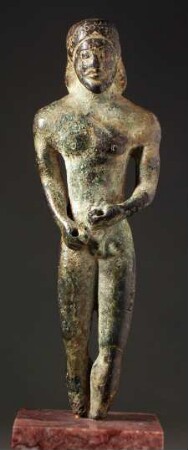 Archaische Statuette eines bärtigen Mannes, bis auf die Füße wohl erhalten. Beide Hände zusammen vor dem Unterleib, beide durchbohrt, Nase abgestoßen