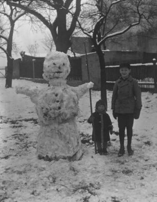 Junge mit Kleinkind neben einem Schneemann stehend