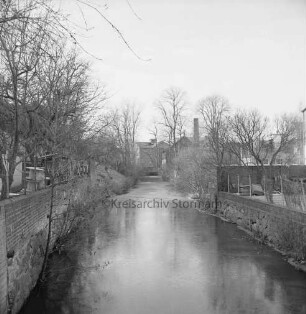 Trave: Stadtarm: Blick von Fußgängerbrücke Richtung Kornwassermühle: rechts und links Mauern und Bäume: hinten Gebäude