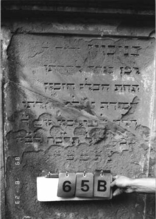 Grabstein 65 (Index: 100110832) Material: Sandstein Zustand: stark verwittert mit Abschieferungen, geringer Textverlust, beschädigt, in der Mitte auseinandergebrochen und wieder zusammengesetzt, schwarz ausgemalte Schrift Maße HxBxT: 159x101x28 cm Beschreibung: Stele, Rundbogenabschluß mit Rundbogenfries und Verdachung, Schriftfelder eingetieft: Grabstein 65B