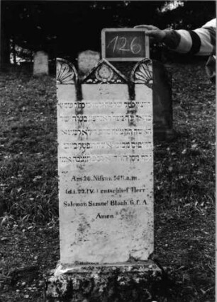 Grabstein 126 (Index: 100090314) Material: weißer Marmor Zustand: gut Maße HxBxT: 127x50x12 cm Beschreibung: Stele, profilierter Sockel, giebelartiger Abschluß mit Akroteren Symbolik: Kranz mit Schleife, Blütenviertel in den Akroteren: Grabstein 126