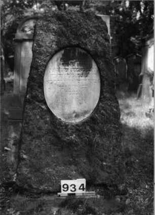 Grabstein 934 (Index: 99630426) Material: Granit mit weißer Marmorplatte Zustand: Schriftplatte verwittert Maße HxBxT: 116x66x44 cm Beschreibung: grob stelenhaft behauener Stein mit Segmentbogenabschluß und ovaler Schriftplatt: Grabstein 934