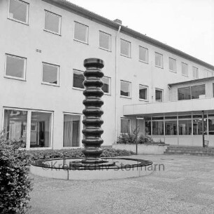 Ahrensburg: Hermann-Löns-Straße: Außenanlagen: Kunst am Bau: Brunnenplastik Betonsäule von Großenseer Künstler Harald Duwe: Blumenbeete, Parklampe: hinten Erweiterungsbau, rechts Verbindungstrakt zum Altbau