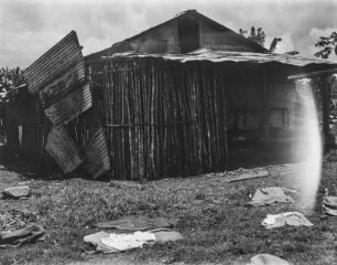 Ein Haus : Ein mit Wellblech gedecktes Haus, auf dem Rasen Wäschestücke.