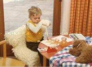 Stark verletztes Kind mit bandagierten Armen beim Malen an einem Tisch (Altersgruppe 18-21)