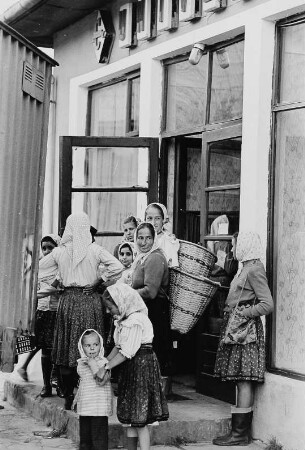 Frauen und Kinder mit Körben vor einem Geschäft