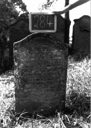 Grabstein 284 (Index: 100103167) Material: Sandstein Zustand: stark verwittert, weitgehender Textverlust Maße HxBxT: 91x50x9 cm Beschreibung: Stele, Konvexbogenabschluss, Schriftfeld durch umlaufende Rille abgeteilt: Grabstein 284